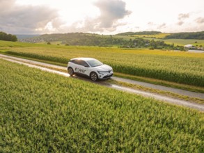 A car moves along a path through green fields with a wide view of the landscape, Deer E-