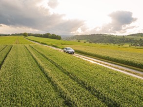 Country lane with a car, surrounded by cornfields and a dramatic sky, Deer E- CarSharing, Renault
