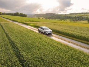 A modern car on a path through agricultural fields under a cloudy sky, Deer E- CarSharing, Renault