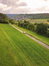 Car on a long journey through green fields, hills and villages in the background, Deer E-