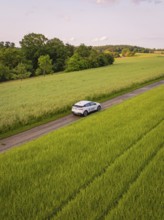 Car drives through rural route surrounded by green fields and summer landscape, Deer E- CarSharing,