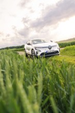 White car surrounded by vegetation and fields under a partly cloudy sky, Deer E- CarSharing,