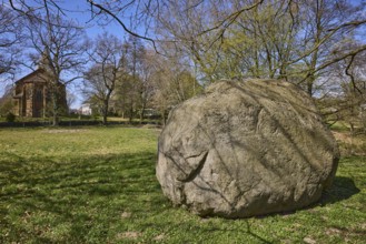 Boulder from southern Sweden, granite, Saale Ice Age, lawn, bare winter trees, blue cloudless sky,