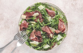 Fresh arugula salad with prosciutto and grated parmesan cheese, on a plate, homemade, no people