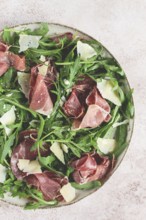Fresh arugula salad with prosciutto and grated parmesan cheese, on a plate, homemade, no people
