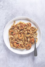 Fettuccine pasta with shrimp, spicy in soy sauce, on a grey plate with a fork, close-up