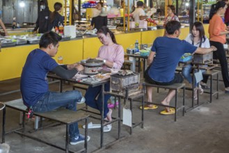 Thai couple cooking on a hot pot and eating at a buffet style outdoor restaurant in Chiang Rai