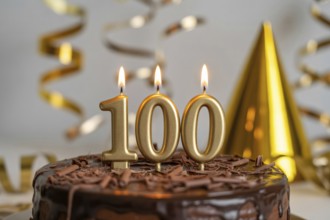 Chocolate cake with golden candles spelling 100. Celebration of longevity and reaching 100 years