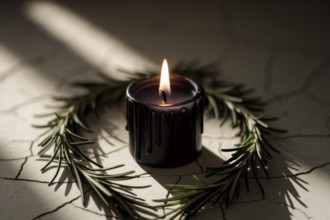 Short black candle burning on cracked stone with rosemary. A symbol of witchcraft, ritual, and