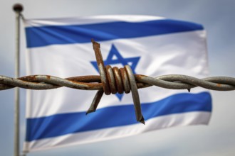 Rusty barbed wire in sharp focus with waving Israeli flag in blurred background. Symbol of