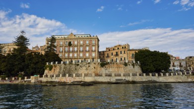 Large historic facades with manicured trees on an elevated coastline, boat trip around the island