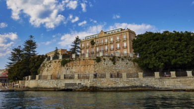 Magnificent building on a cliff, surrounded by lush vegetation and clear skies, boat trip around
