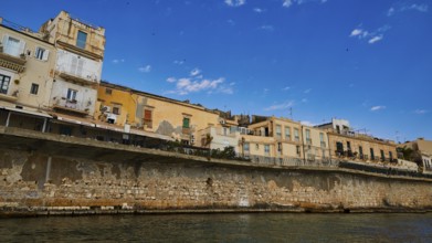 Row of historic houses on a stone seawall under a clear sky, boat trip around the island of