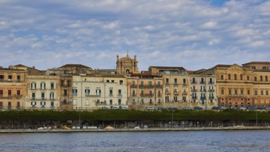 Rows of historic buildings along a coastal promenade under a patterned sky, boat trip around the