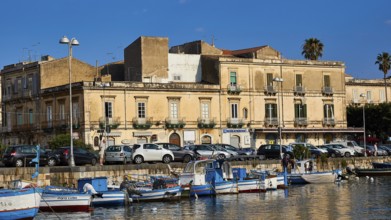 Fishing boats in a harbour in front of historic buildings and parked cars, boat trip around the