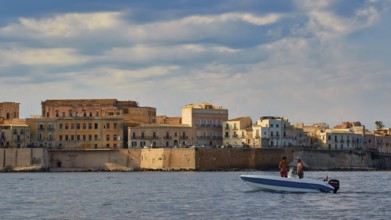 Boat with two people in front of historic coastline and cloudy sky, boat trip around the island of