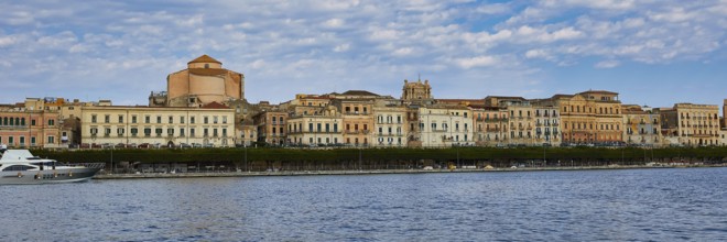 Coastal view with historic buildings against a cloudy blue sky on the promenade, boat trip around