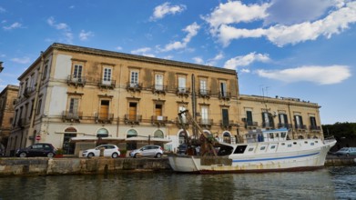 Historic coastal building with parked boat under a blue sky, boat trip around the island of