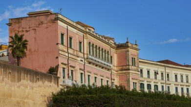 Pink historic building with many windows under a blue sky, Ortigia Island, Isola di Ortigia,