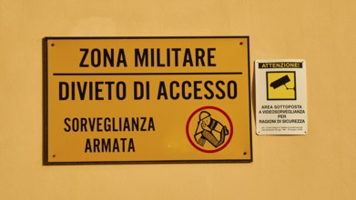 Warning sign on a wall indicating a military zone with restricted access and surveillance, Ortigia