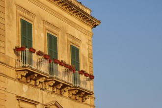 Facade of a building with balconies and green shutters in the sunlight, Ortigia Island, Isola di