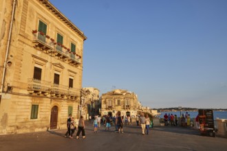 People and historic buildings on a sunny town square in the evening, Ortigia Island, Isola di
