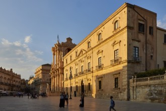 Large building with classical architecture on a sunny square with passers-by, Ortigia Island, Isola