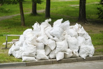 Multiple white heavy-duty garbage bags filled with waste material are piled up in a green park area