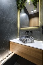 A sleek bathroom with a striking stone sink mounted on a wooden cabinet. The walls are tiled with