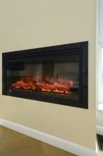 An electric fireplace is set into a wall in a bright living room. Flickering flames illuminate the