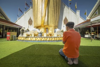 Man praying in front of a 32 metre high standing Buddha decorated with glass mosaics and 24 carat