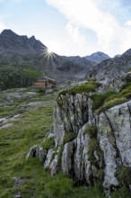 Mountain hut Elberfelderhütte in front of a rocky mountain landscape, sun star in the morning, in