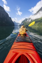 Kayak trip on the Geirangerfjord, young woman paddling in a red kayak, atmospheric fjord landscape,