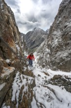 Mountaineer on a rope-secured path in a steep rocky mountain landscape with fresh snow in summer,