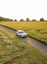 Electric car driving on a lonely country road between wide grain fields in the sunset, Renault