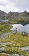 Mountaineer on a rock in front of mountain lakes Wangenitzsee and Kreuzsee, cloudy mountain peaks
