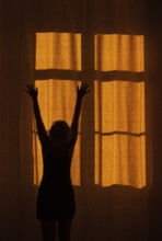 Back view of a woman with raised hands standing in front of a window with a red curtain