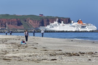 Tourists and photographers on the beach of the Heligoland dune, cruise ship in front of cliffs,
