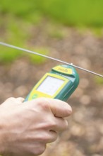 Hand holding an electronic device near a wire fence, Waldweide Gechingen, compensation project for
