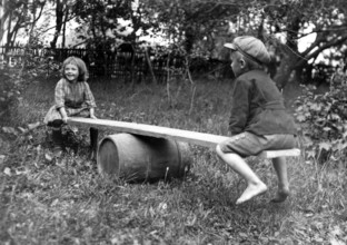 Two children swinging in the garden, 1930s, Two children playing happily on an improvised seesaw in