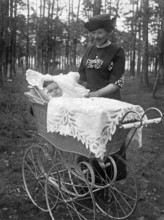 Couple with baby in pram, 1910s, woman in vintage dress next to a pram in the forest. A baby lies