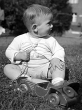 Little boy playing with a wooden car, 1930s, Toddler sitting in the grass and playing with a red