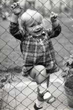Little girl climbing over the fence, 1930s, child in a chequered dress, holding on to the fence,