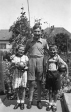 Siblings with big brother, 1950s, Three children posing with balls in a garden and smiling at the