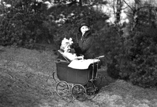 Girl playing with doll, 1920s, Woman with hat and fur collar pushing an antique pram in the forest,