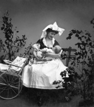Motherly love, mother breastfeeding baby, 1930s, mother breastfeeding baby next to a cart, black