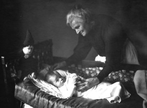Grandma with grandson, 1930s, An elderly woman lovingly cares for a baby in a cradle, Historical