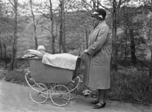 Woman pushing pram, 1920s, Woman with hat standing next to a pram and laughing with the baby lying