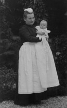 Nanny holding a baby in her arms, ca. 1910, Woman in Victorian dress holding a baby in the garden,