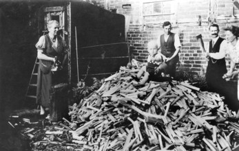 Baby sitting on a mountain of firewood, 1930s, family working together in the yard chopping wood